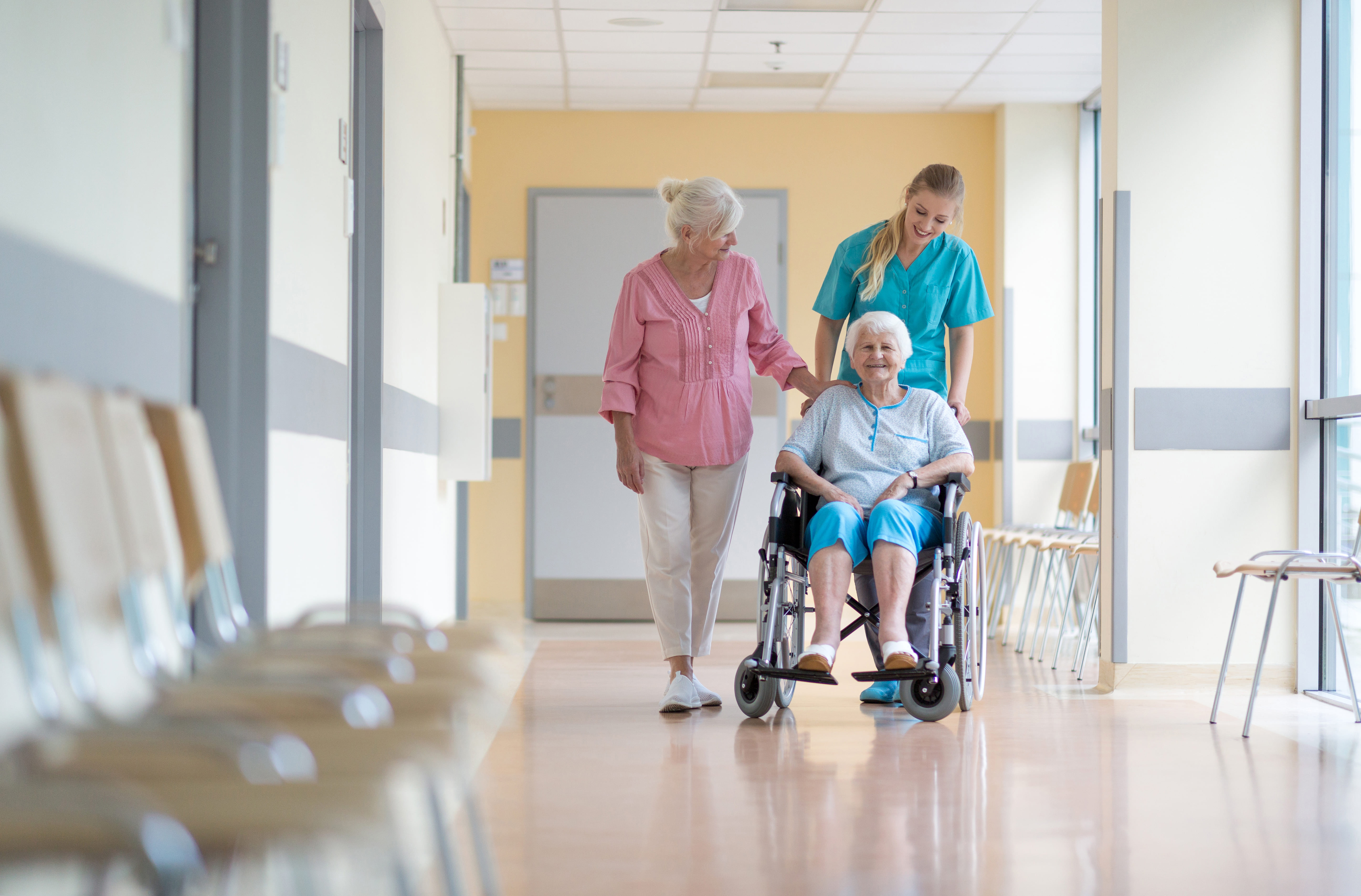 une infirmière pousse une dame âgée en fauteuil roulant dans un Ehpad