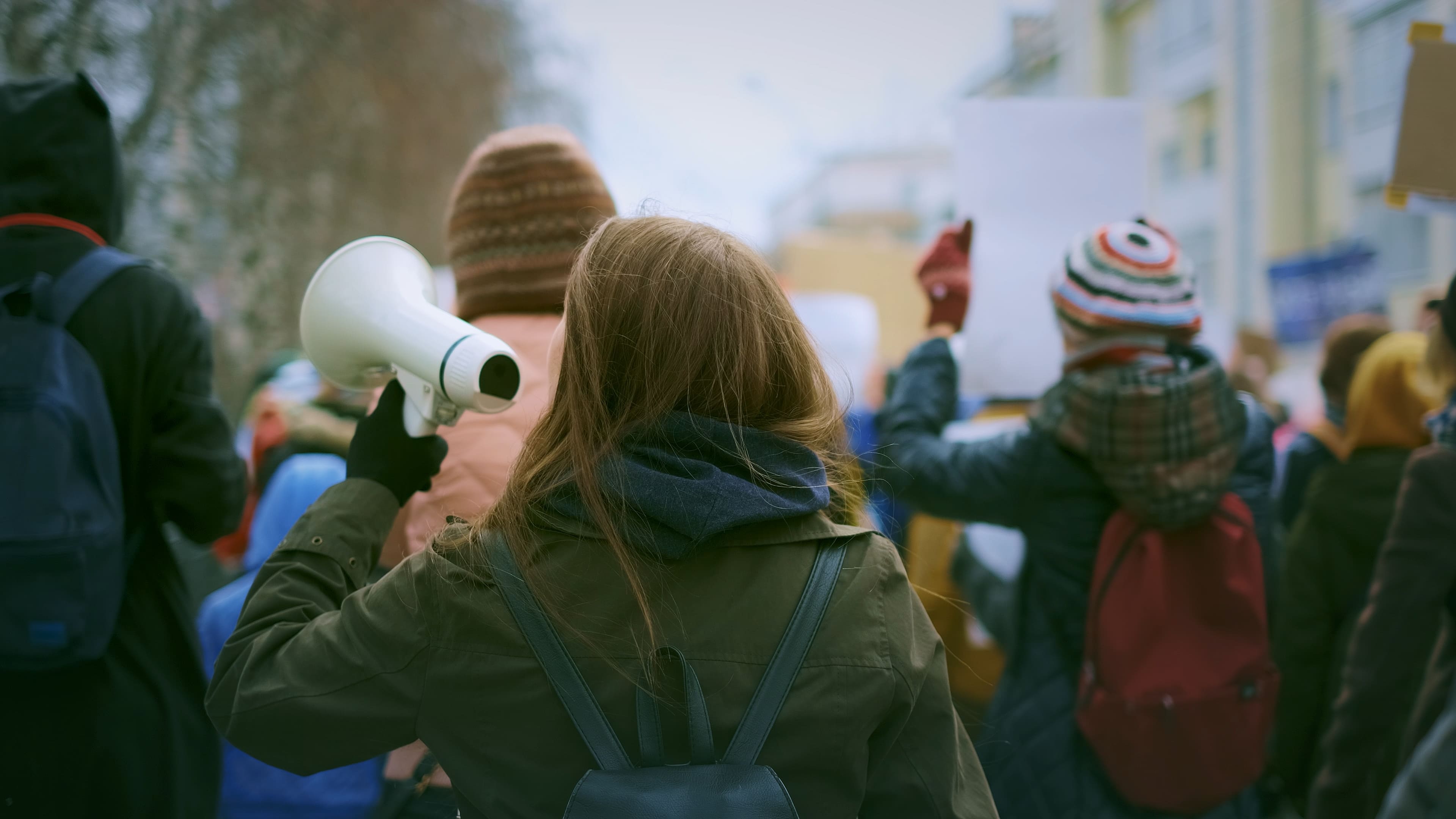 une femme de dos manifeste avec un haut parleur