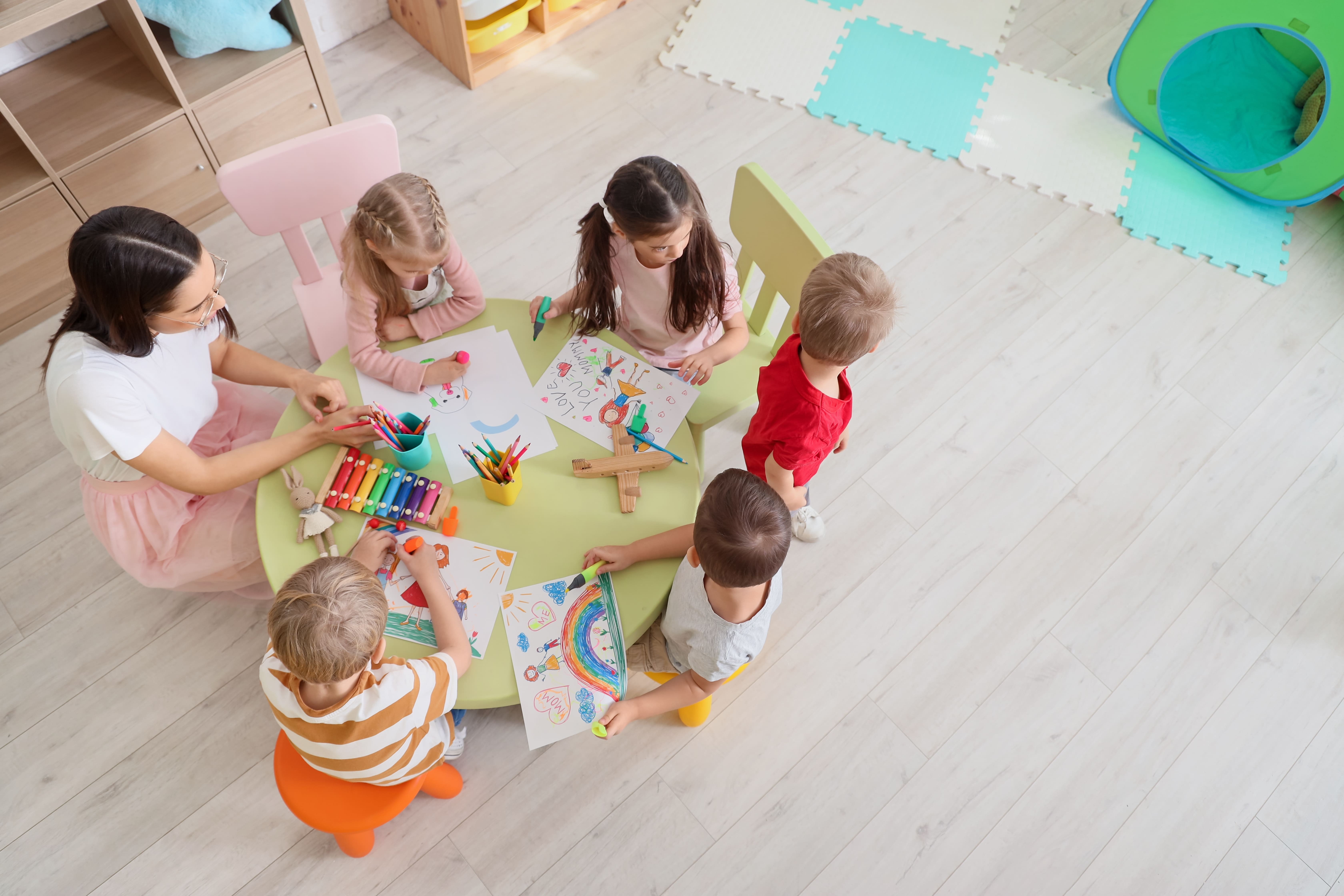 des enfants et une auxiliaire de puériculture font des dessins dans une crèche